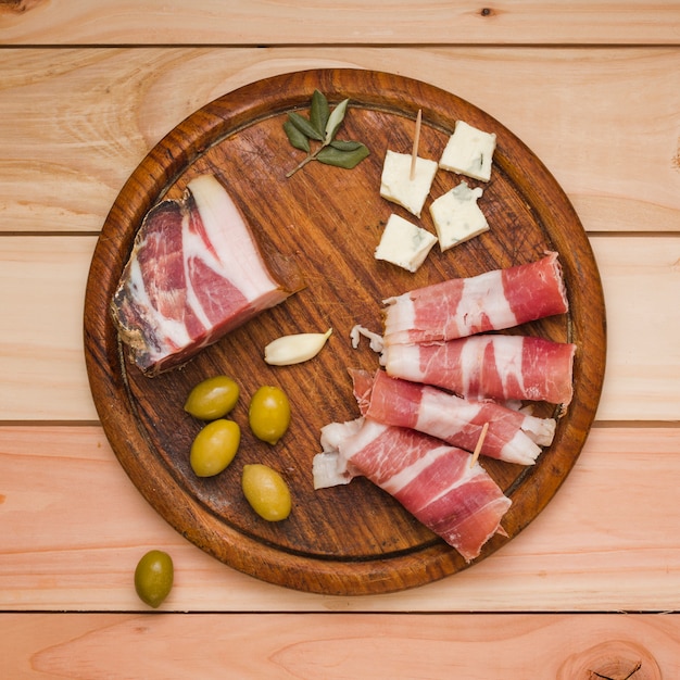 Olives; garlic clove; cheese slice and bacon on wooden tray over the desk