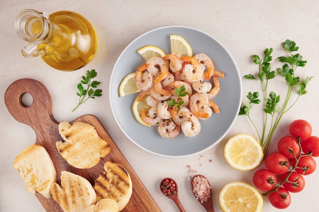 Olives, oil, Grilled shrimps and fresh vegetable salad on a wooden board on black slate stone board over light surface, juicy tomatoes on fresh bread, pesto as topping. top view. Flat lay