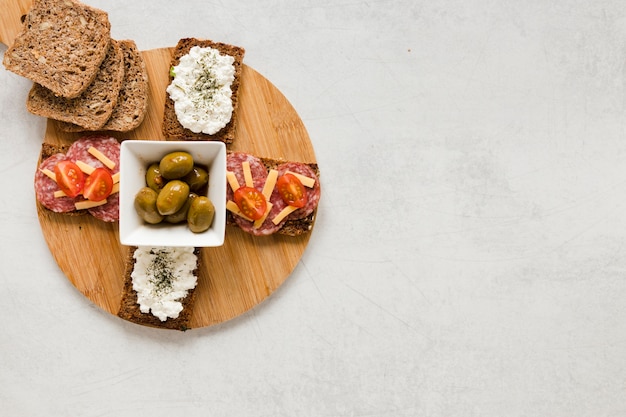 Olives and sandwiches on cutting board with copy space