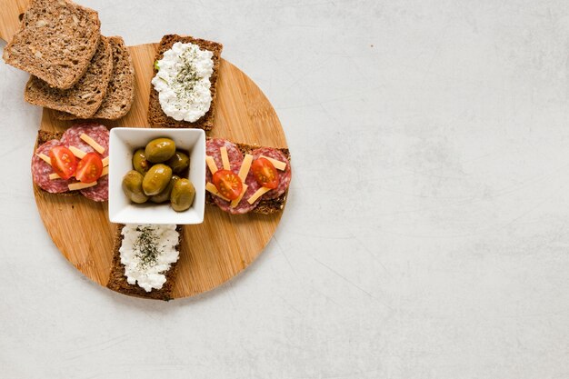Olives and sandwiches on cutting board with copy space