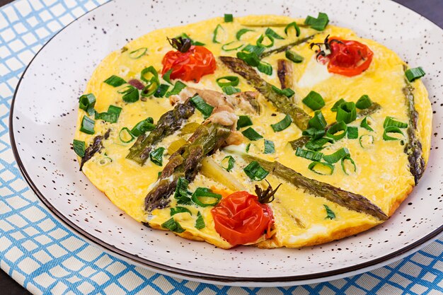 Omelette with asparagus and tomato for breakfast on a wooden table.
