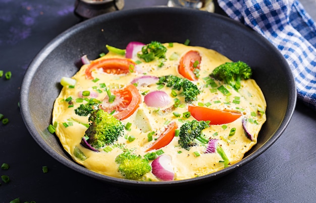 Omelette with broccoli,  tomatoes and red onions in iron skillet. Italian frittata with vegetables.