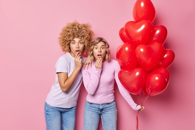 Omg san valentino sta arrivando scioccato due donne fissate impressionate prepararsi per la festa tenere un mazzo di palloncini a forma di cuore rosso isolati su sfondo rosa evento festivo e concetto di celebrazione