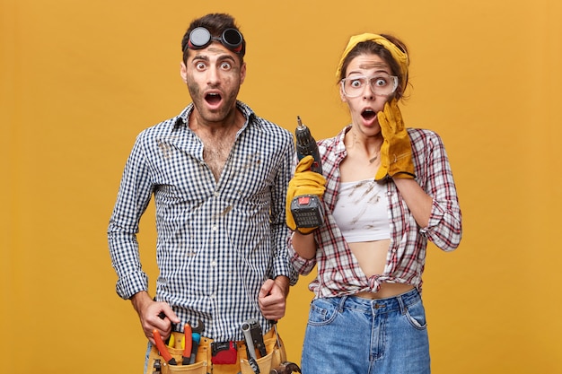 Omg! Wow! portrait of emotional surprised young European service technicians wearing safety goggles looking in full disbelief, keeping mouths wide opened and eyes popped out