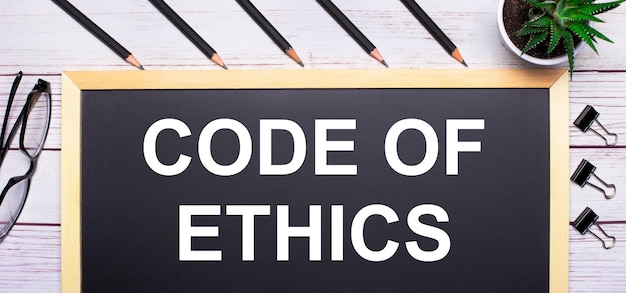 На светлом деревянном столе - доска с текстом кодекс этики, карандаши, растения, стаканы и скрепки. бизнес-концепция