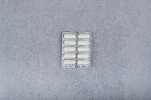 One blister with white pills on gray surface