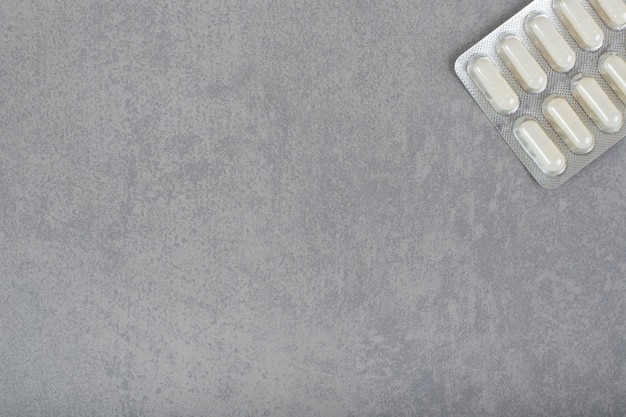 One blister with white pills on gray surface