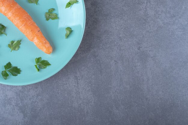 One carrot on the plate whit greens, on the marble surface.