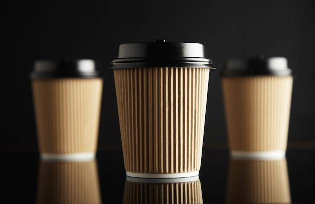 One focused in front of unfocused brown take away cardboard paper cups closed with caps isolated on black and mirrored. Retail  presentation