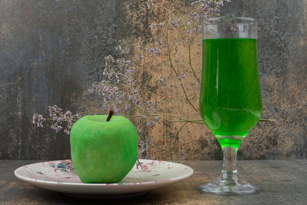 One fresh green apple with glass of green water on dark plate. 