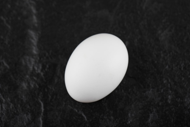 One fresh white chicken egg on a black table .