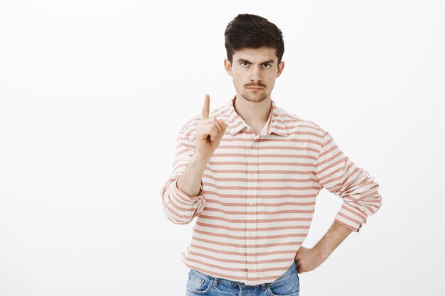 One more thing. Indoor shot of displeased angry european man with moustache and beard, shaking index finger and frowning from displeasure and annoyance