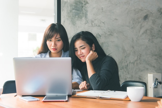 Free photo one-on-one meeting.two young business women sitting at table in cafe. girl shows colleague information on laptop screen. girl using smartphone blogging. teamwork business meeting. freelancers working.