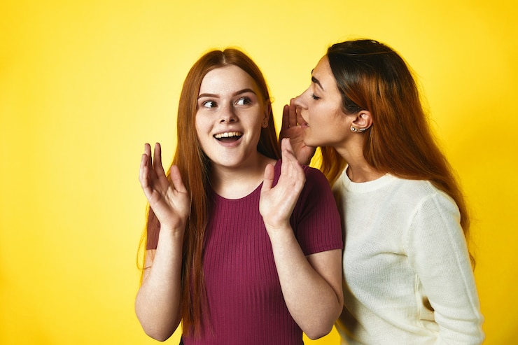 Free Photo one redhead girl is whispering to another caucasian girl in the ear