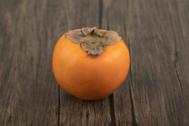 Один спелый плод хурмы на деревянной поверхности