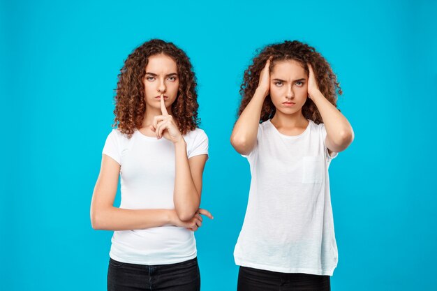 One of sisters twins showing keep silence over blue.