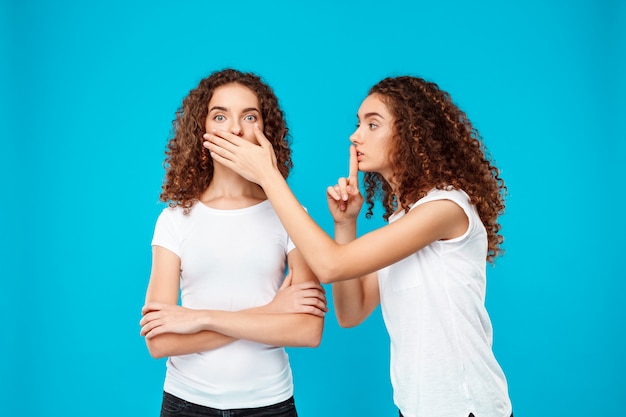one of sisters twins showing keep silence over blue.