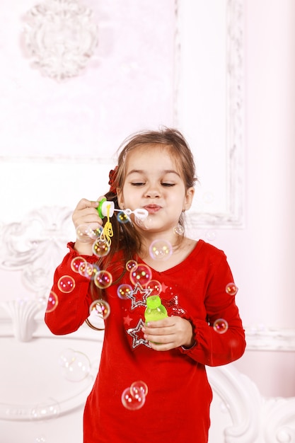 One small girl dressed in red pajamas is playing with bubbles indoors