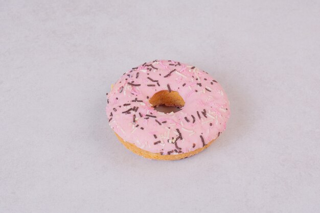 Один сладкий розовый пончик на белой поверхности