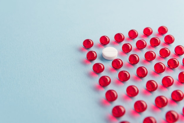 One white round tablet in a grid of red capsules