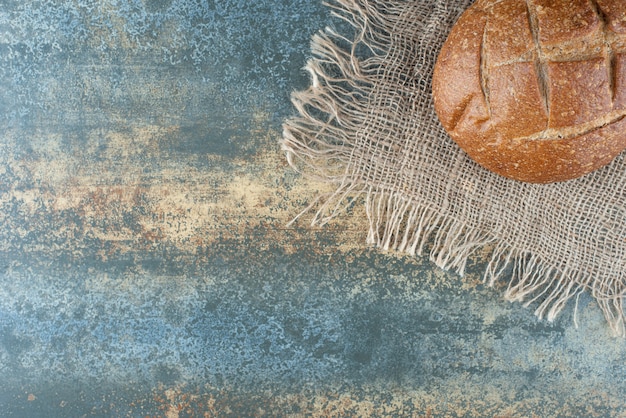 Foto gratuita un intero panino marrone fresco su tela di sacco