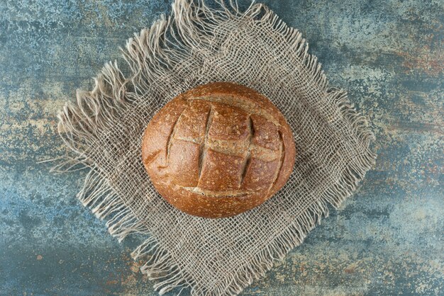 Free photo one whole fresh brown bun on sackcloth