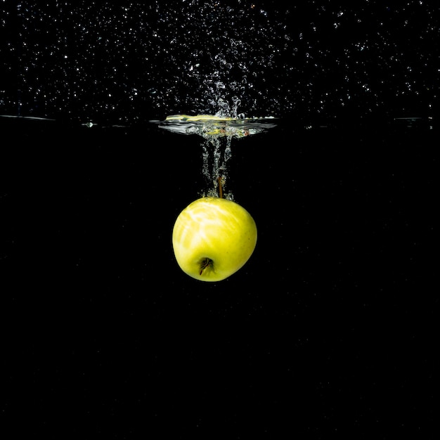One whole green apple splashing into water against black background
