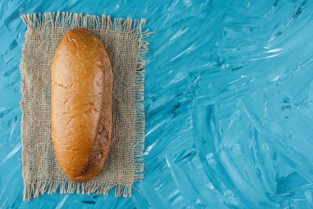 Foto gratuita una pagnotta intera di pane fresco bianco su tela di sacco su sfondo blu.