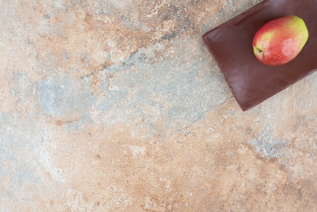 One whole red sweet apple on dark plate .