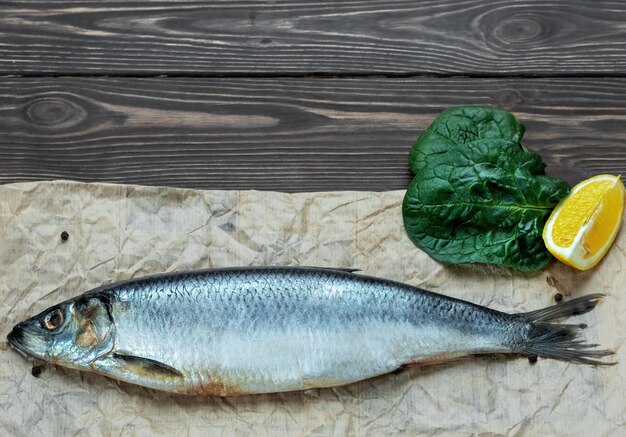 One whole salted atlantic herring on parchment paper, next to spices, lemon and lettuce leaf