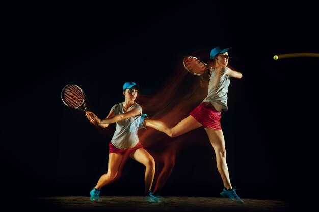 混合光とストーブ光で黒い壁に隔離されたさまざまな位置でテニスをしている一人の女性