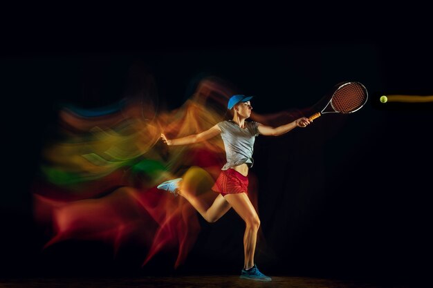 混合とストーブの光の中で黒い壁に隔離されたテニスをしている一人の女性