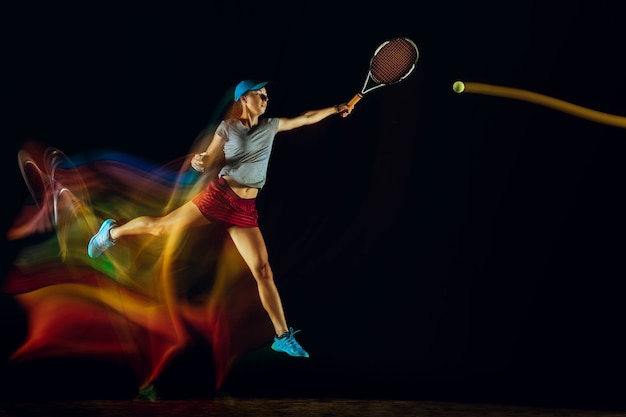One woman playing tennis isolated on black wall in mixed and stobe light