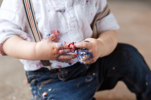 One year old kid after eating a slice of birthday smash cake by himself getting dirty. 