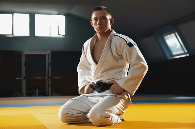 Один молодой боец в кимоно тренирует боевые искусства в спортзале