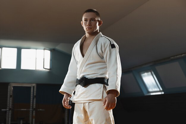 One young fighter in kimono training martial arts in the gym