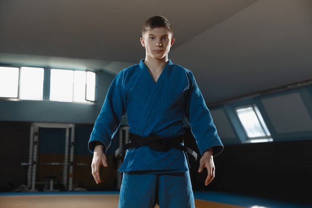 One young fighter in kimono training martial arts in the gym