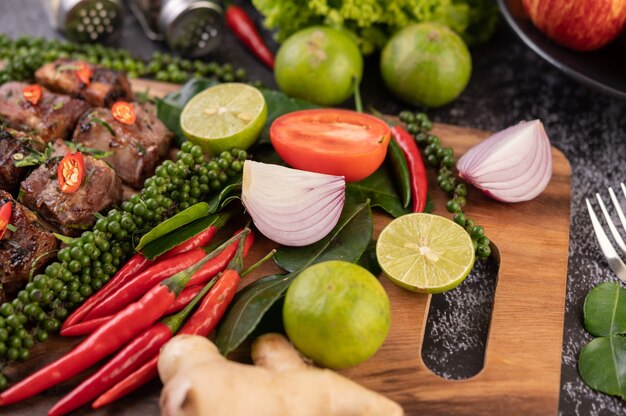 Onion, chili, fresh pepper Kaffir lime leaves and lime placed on a wooden chopping board.