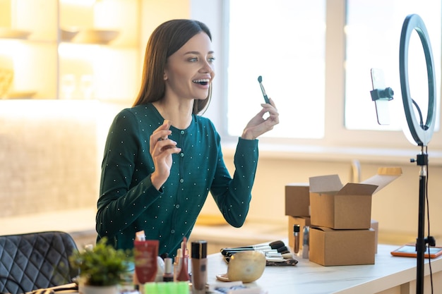 Foto gratuita corso di bellezza online. giovane donna in abito verde che mostra consigli per il trucco online