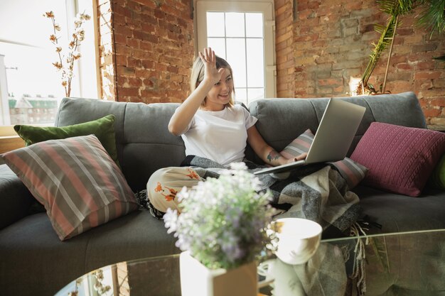 Online conference. Caucasian woman, freelancer during the work in home office while quarantine. Young businesswoman at home, self isolated. Using gadgets. Remote work, coronavirus spread prevention.