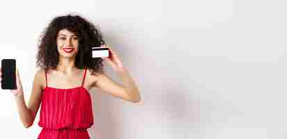 Free photo online shopping concept elegant female model with curly hair wearing red dress showing plastic credi