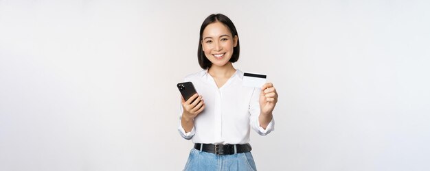 現代のアジアの女の子の笑顔のオンラインショッピングの概念は、彼女のクレジットカードが携帯電話の注文ウィットを保持していることを示しています