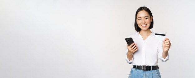 現代のアジアの女の子の笑顔のオンラインショッピングの概念は、彼女のクレジットカードが携帯電話の注文ウィットを保持していることを示しています