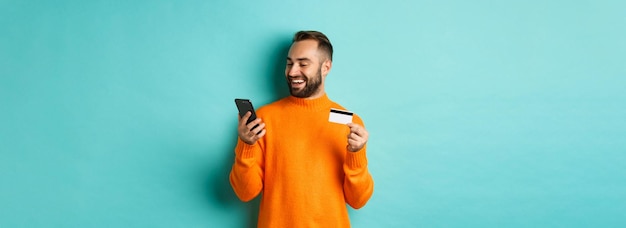 Foto gratuita shopping online bell'uomo barbuto che paga in internet tenendo la carta di credito e fissa lo scre mobile