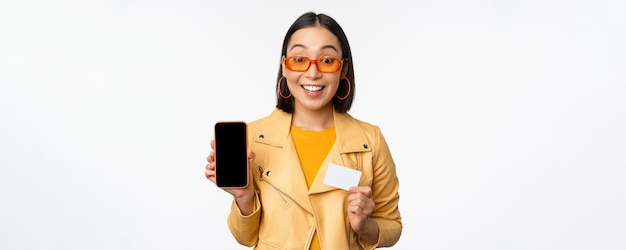 オンラインショッピングと人々のコンセプト携帯電話の画面とクレジットカードを表示するスタイリッシュなアジアの女性