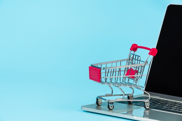 Online shopping , a shopping cart placed alongside a notebook on a blue  .