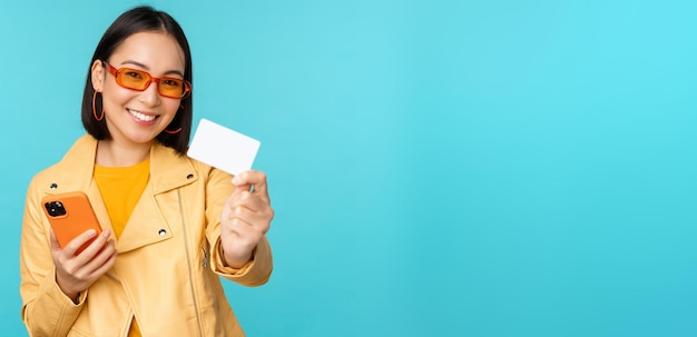 신용 카드를 보여주고 스마트폰 지불을 사용하는 선글라스를 쓴 세련된 젊은 아시아 여성 온라인 쇼핑