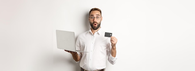 L'acquisto in linea ha sorpreso l'uomo che tiene il negozio di internet del negozio del computer portatile e della carta di credito che sta sopra il bianco