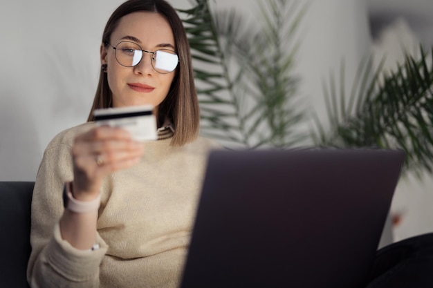 카드 및 노트북을 사용한 온라인 쇼핑 기술을 사용하여 실내 소파에 앉아 쇼핑하는 백인 여성