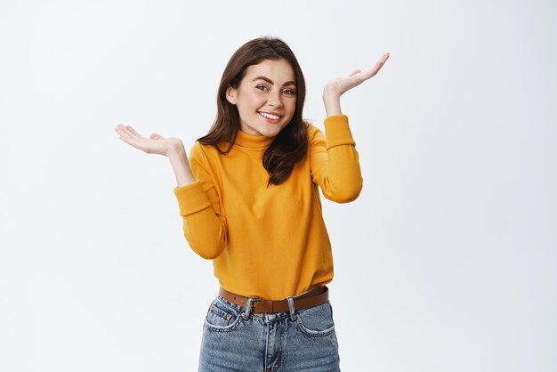 Oops my mistake Cute silly girl raising hands up and shrugging confused smiling as being little guilty dont know how it happened standing against white background